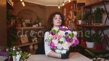 年轻女子在花店当花店花店工，看着相机，书桌上放着花束微笑